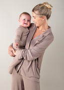 Woman holding a baby and both wearing matching beige outfits against a plain background
